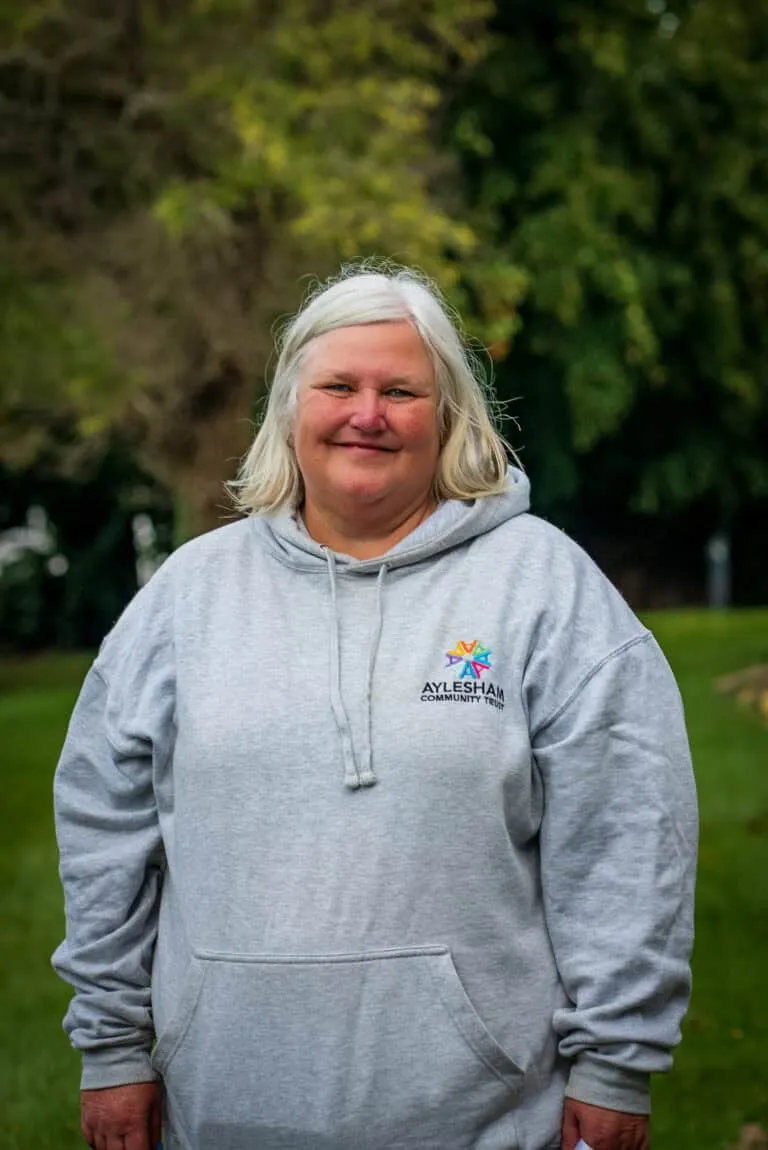Aylesham community trustee woman smiling outdoors in a grey hoodie with community trust logo.