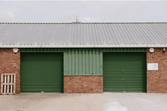Bright green metal garage doors at Aylesham Community Trust building in a peaceful, community-focused setting with brick walls and a corrugated metal roof.