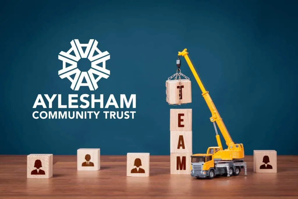 Community trust logo with construction crane lifting wooden blocks spelling 